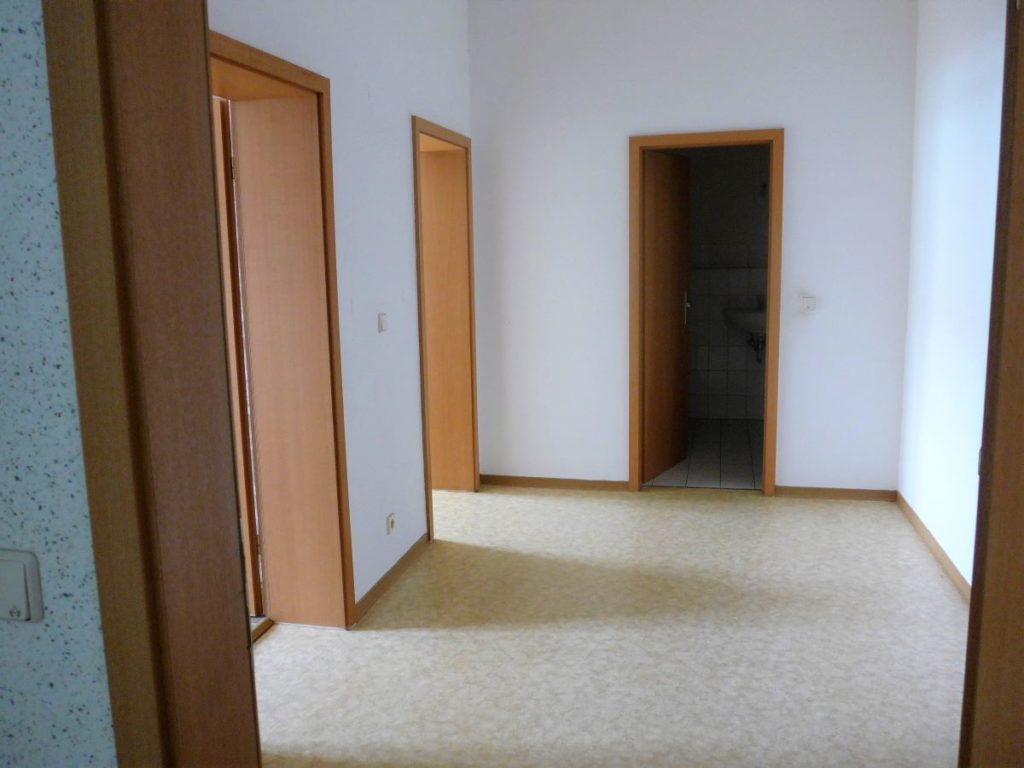 Flur mit weißen Wänden, beigen PVC Bodenbelag, 3 buchefarbene Zimmertüren von Bad, Küche und Wohnzimmer