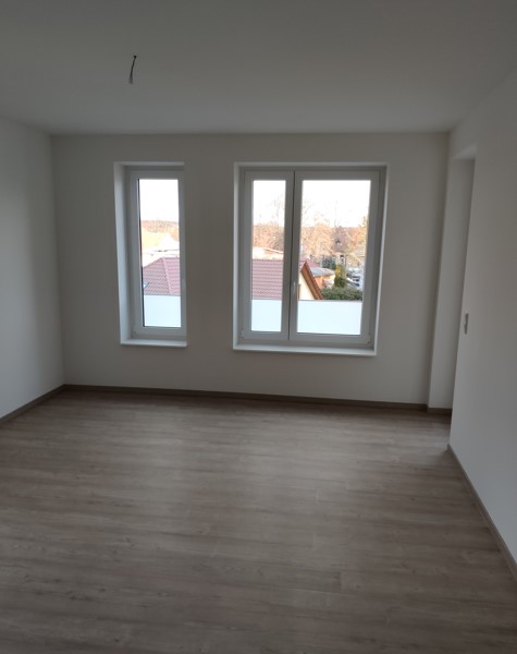 Feistkornstraße 9a 1 helles, lichtdurchflutetes Wohnzimmer mit einem Doppelfenster und einen Einzelfenster, Zugang zum Balkon und grau/beigen Bodenbelag mit weißen Wänden