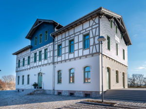 Außenansicht des historischen Bahnhofsgebäudes Kölleda mit Fachwerkelementen und neu gestalteter Außenanlage; die Caféfläche liegt im Erdgeschoss zur Platzseite.