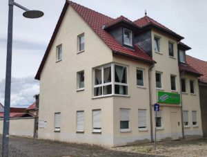 Das Bild zeigt ein mehrstöckiges, hell verputztes Gebäude m mit rotem Ziegeldach und Fenstergauben im Dachgeschoss, das an einer Straßenecke steht.