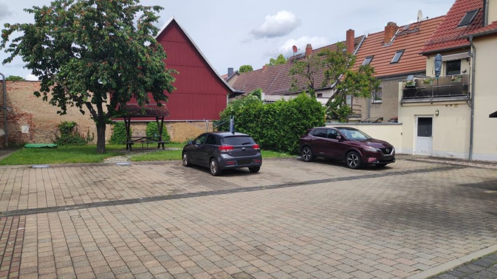 Brückentor 1 2 Das Bild zeigt einen weitläufig geplasterten Innenhof mit Grünfläche, einer Sitzgelegenheit, einem Kirschbaum und Wäscheständern. Im Innenhof befinden sich mehrere Pkw Stellplätze. Der Innenhof ist umgeben von Gebäuden.
